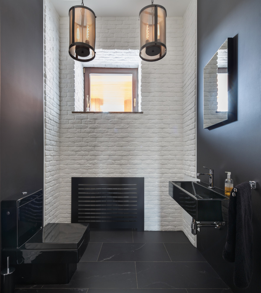 Exempel på ett modernt toalett, med ett väggmonterat handfat, svarta väggar, en toalettstol med hel cisternkåpa och svart golv