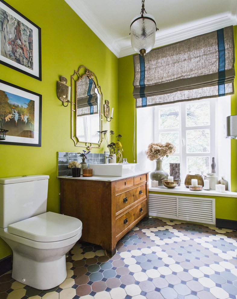 На фото: туалет в стиле фьюжн с плоскими фасадами, фасадами цвета дерева среднего тона, раздельным унитазом, зелеными стенами, настольной раковиной и разноцветным полом