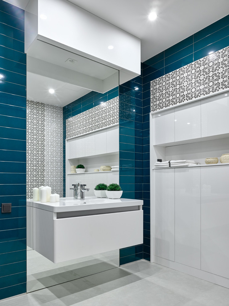 Стильный дизайн: туалет среднего размера в современном стиле с плоскими фасадами, белыми фасадами, синей плиткой, керамической плиткой, синими стенами, полом из керамогранита, монолитной раковиной и белым полом - последний тренд