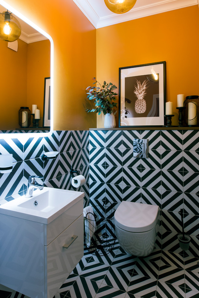 Modern inredning av ett toalett, med släta luckor, vita skåp, en vägghängd toalettstol, svart och vit kakel, orange väggar, ett integrerad handfat och flerfärgat golv