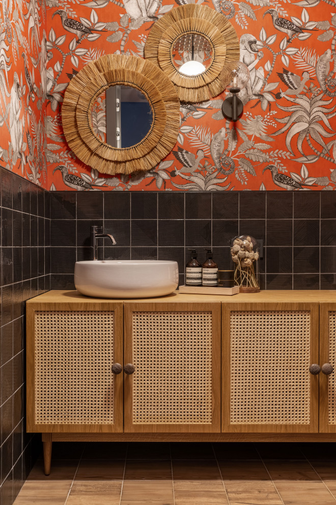 На фото: большой туалет в современном стиле с фасадами с утопленной филенкой, светлыми деревянными фасадами, черной плиткой, керамической плиткой, оранжевыми стенами, полом из керамической плитки, накладной раковиной, столешницей из дерева, коричневым полом, коричневой столешницей, напольной тумбой и потолком с обоями