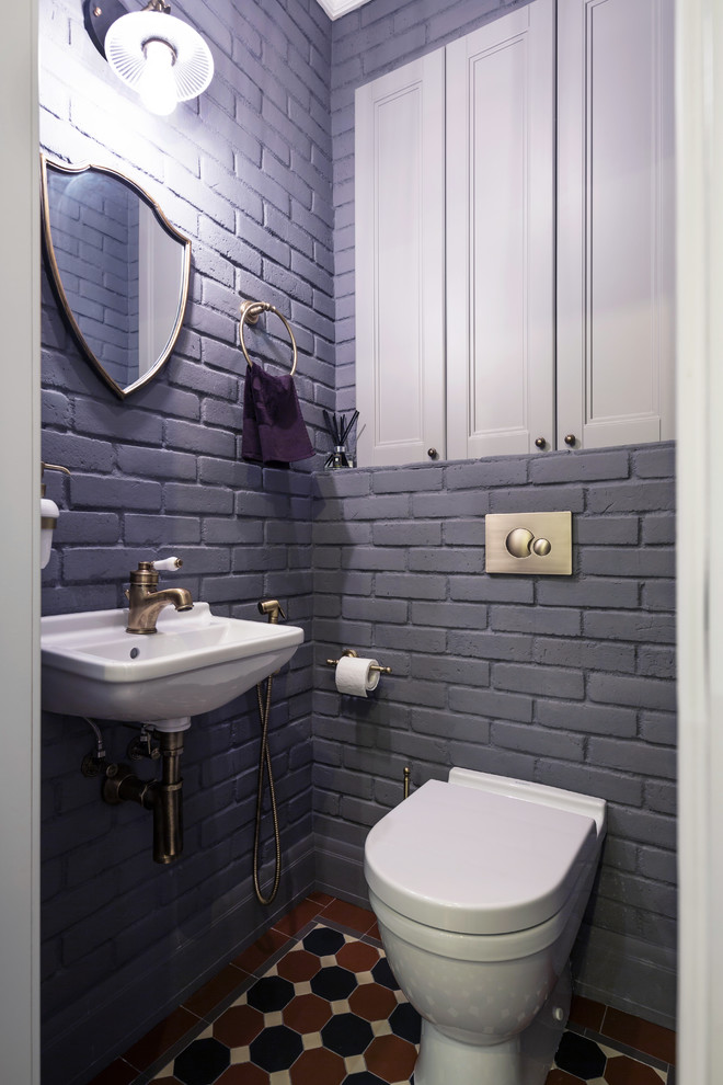 Industriell inredning av ett toalett, med en toalettstol med separat cisternkåpa, grå väggar, ett väggmonterat handfat och flerfärgat golv