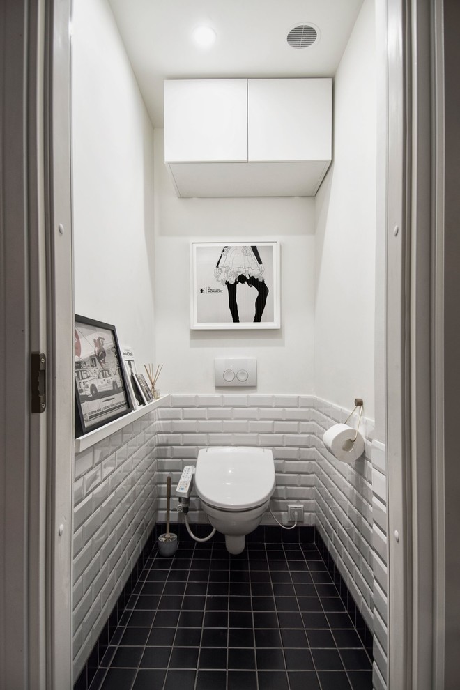 Bild på ett litet nordiskt toalett, med en vägghängd toalettstol, vit kakel, vita väggar, klinkergolv i keramik, tunnelbanekakel och svart golv