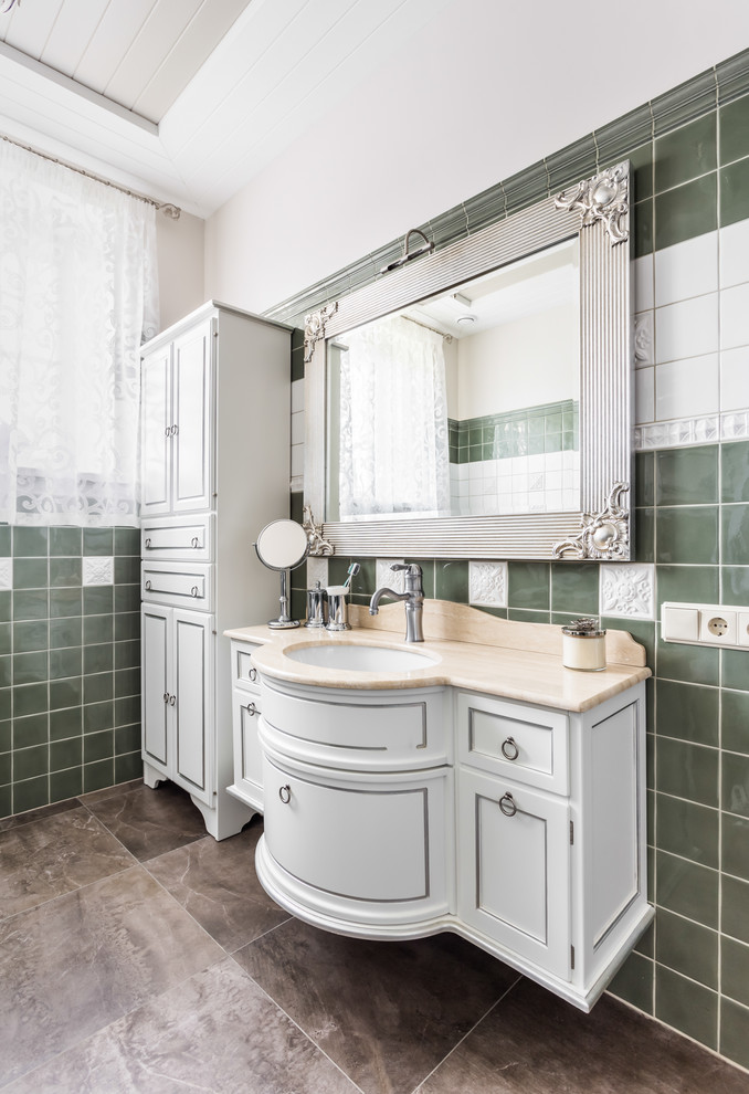 Klassisk inredning av ett mellanstort toalett, med luckor med infälld panel, vita skåp, grön kakel, porslinskakel, vita väggar, klinkergolv i porslin, ett undermonterad handfat och marmorbänkskiva