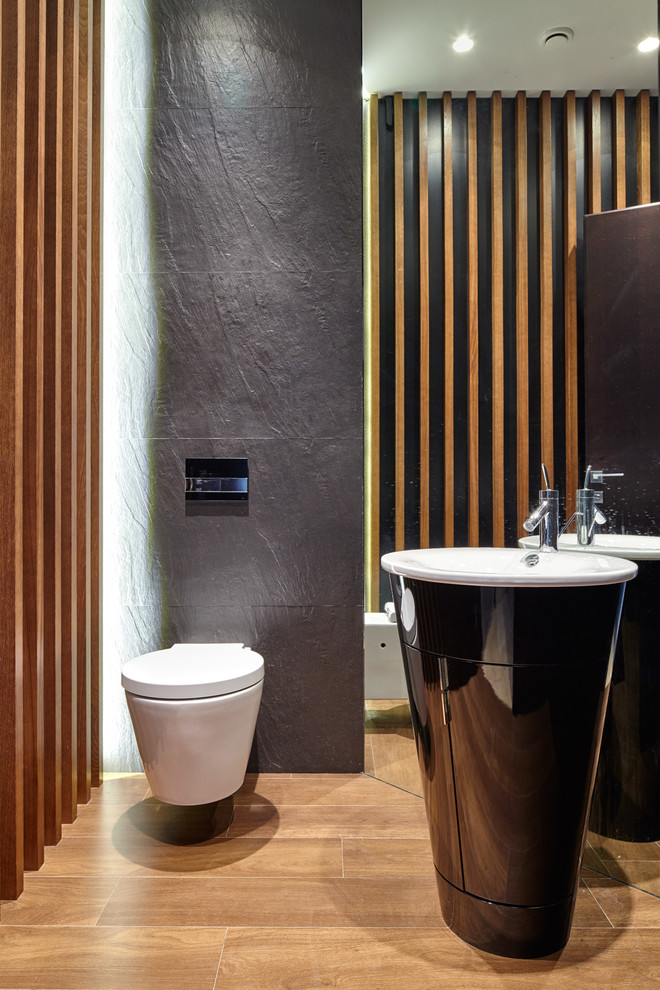 Modern inredning av ett toalett, med en vägghängd toalettstol, grå kakel, grå väggar och ett piedestal handfat