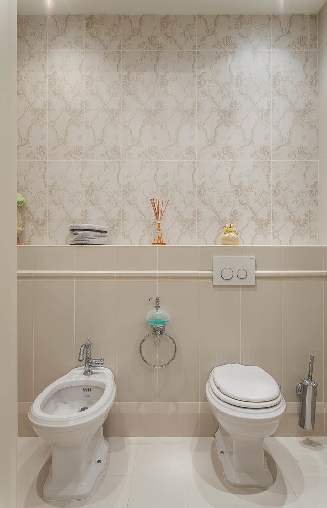 На фото: туалет в классическом стиле с бежевой плиткой, бежевыми стенами, биде и белым полом с