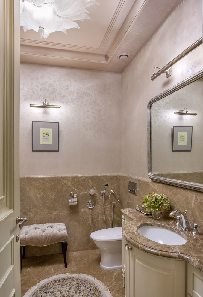 Exemple d'un WC et toilettes chic de taille moyenne avec des dalles de pierre, un mur beige, un sol en marbre, un lavabo encastré, un plan de toilette en marbre, un placard avec porte à panneau surélevé, des portes de placard beiges, un carrelage beige et un sol beige.