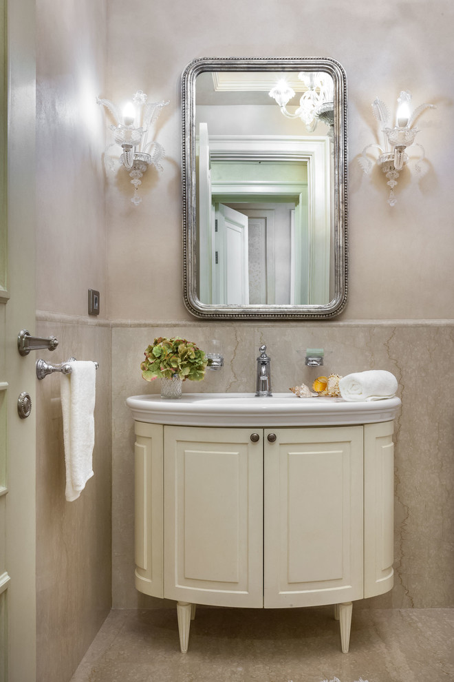 Réalisation d'un WC et toilettes tradition de taille moyenne avec un carrelage beige, des dalles de pierre, un mur beige, un sol en marbre, un placard avec porte à panneau surélevé, un lavabo intégré et des portes de placard beiges.