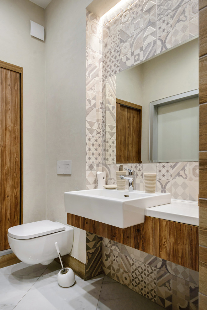 Стильный дизайн: туалет в современном стиле с инсталляцией, серой плиткой, белой плиткой, цементной плиткой, бежевыми стенами, настольной раковиной, бежевым полом и белой столешницей - последний тренд