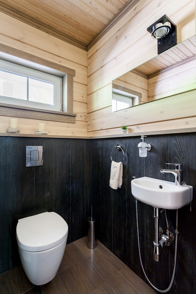Diseño de aseo campestre con sanitario de pared, paredes negras, lavabo suspendido y suelo marrón