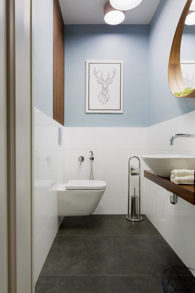 Example of a small danish white tile and porcelain tile gray floor powder room design in Other with flat-panel cabinets, brown cabinets, a wall-mount toilet, a drop-in sink, wood countertops and brown countertops
