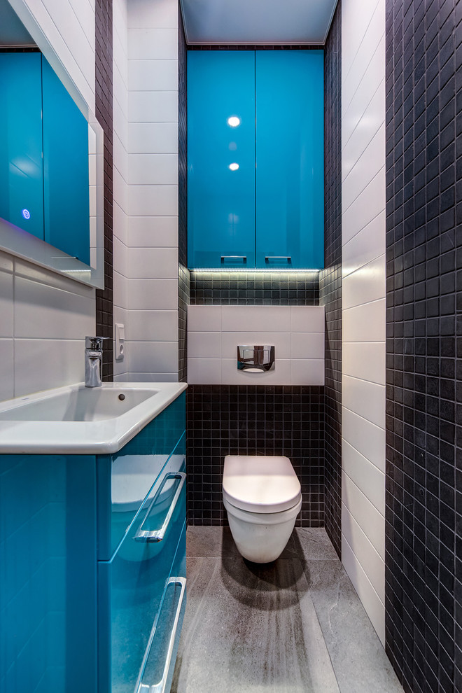 Aménagement d'un WC suspendu contemporain avec un placard à porte plane, des portes de placard bleues, un carrelage blanc, un carrelage noir, un lavabo intégré et un sol gris.