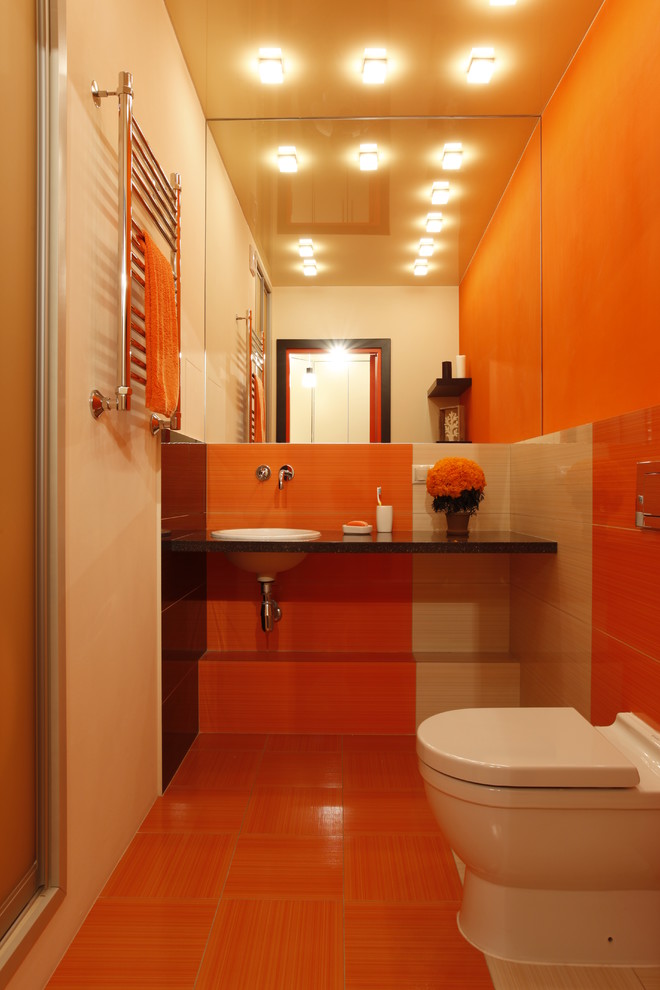 На фото: туалет в современном стиле с столешницей из искусственного камня, раздельным унитазом, накладной раковиной, разноцветной плиткой, оранжевыми стенами и полом из керамической плитки