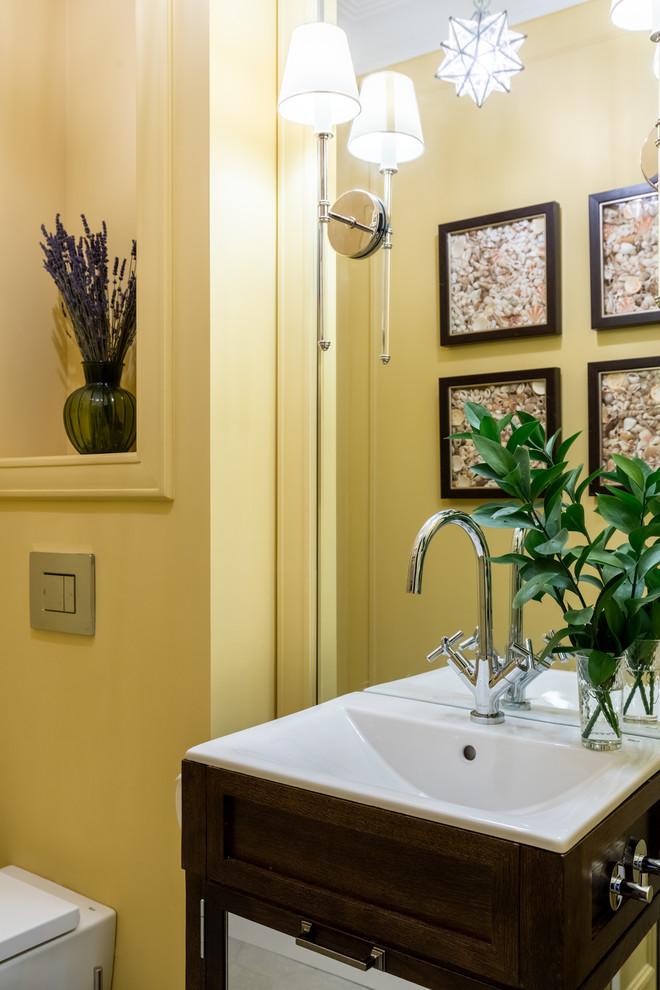 Small traditional cloakroom in Moscow with recessed-panel cabinets, brown cabinets, a wall mounted toilet, yellow walls, ceramic flooring, a built-in sink and beige floors.