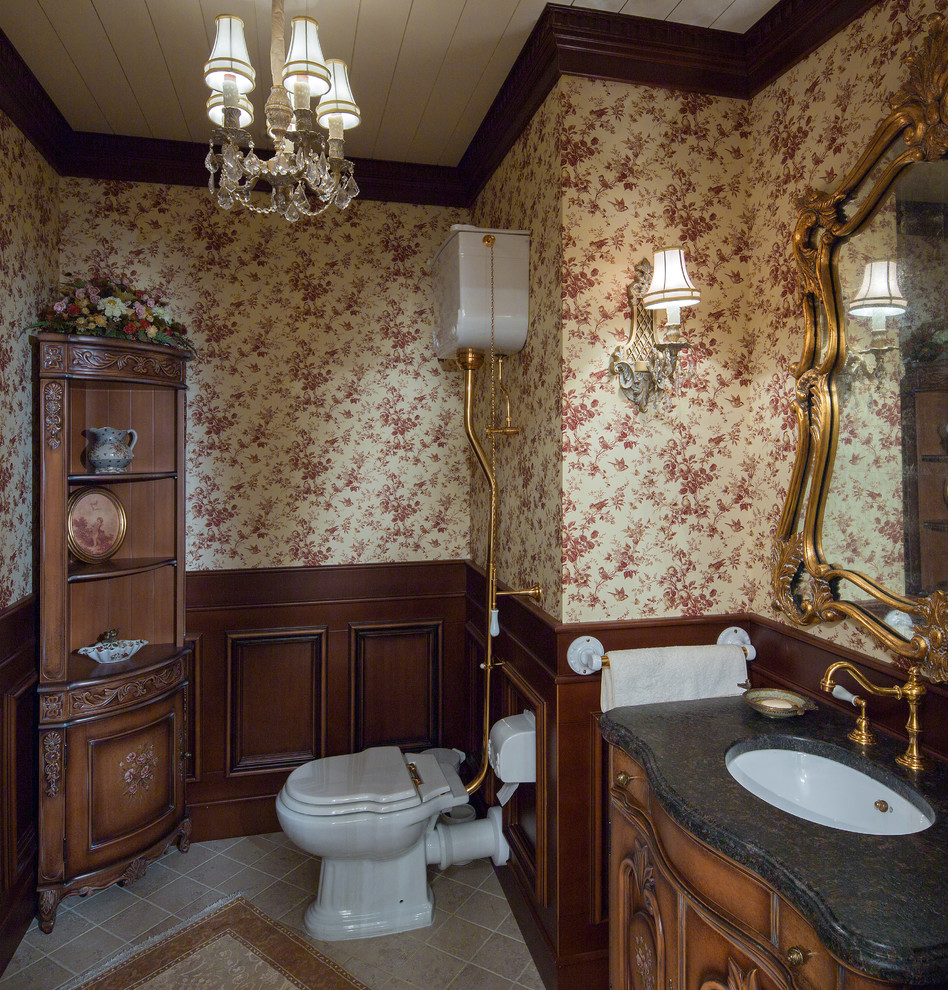 Inredning av ett klassiskt toalett, med skåp i mellenmörkt trä, ett undermonterad handfat, möbel-liknande, flerfärgade väggar och beiget golv