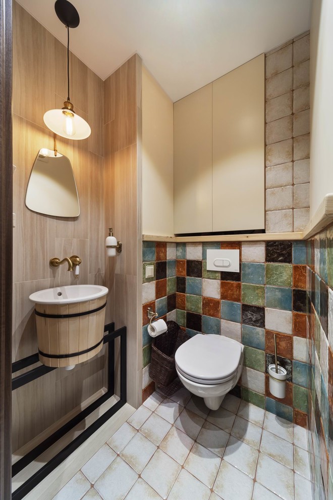 Photo of a contemporary cloakroom in Yekaterinburg with a wall mounted toilet, beige tiles, multi-coloured tiles, a console sink and white floors.