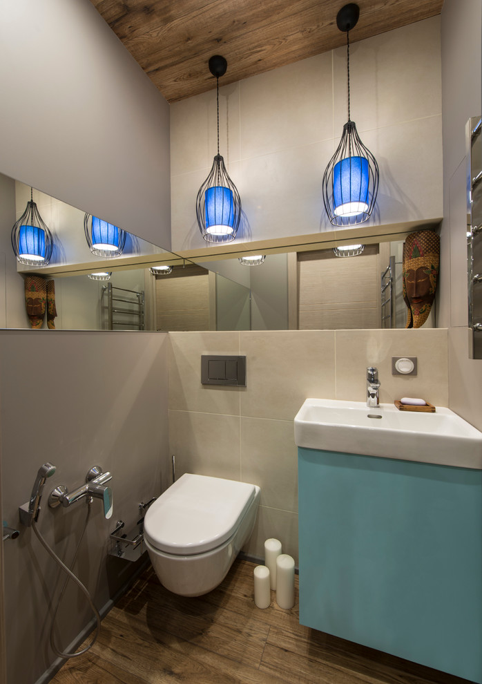 Bild på ett funkis toalett, med släta luckor, blå skåp, en vägghängd toalettstol, beige kakel, grå väggar, mörkt trägolv och brunt golv