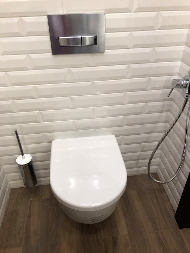This is an example of a small industrial cloakroom in Saint Petersburg with flat-panel cabinets, dark wood cabinets, a wall mounted toilet, white tiles, ceramic tiles, white walls, ceramic flooring, a vessel sink, solid surface worktops, multi-coloured floors and white worktops.