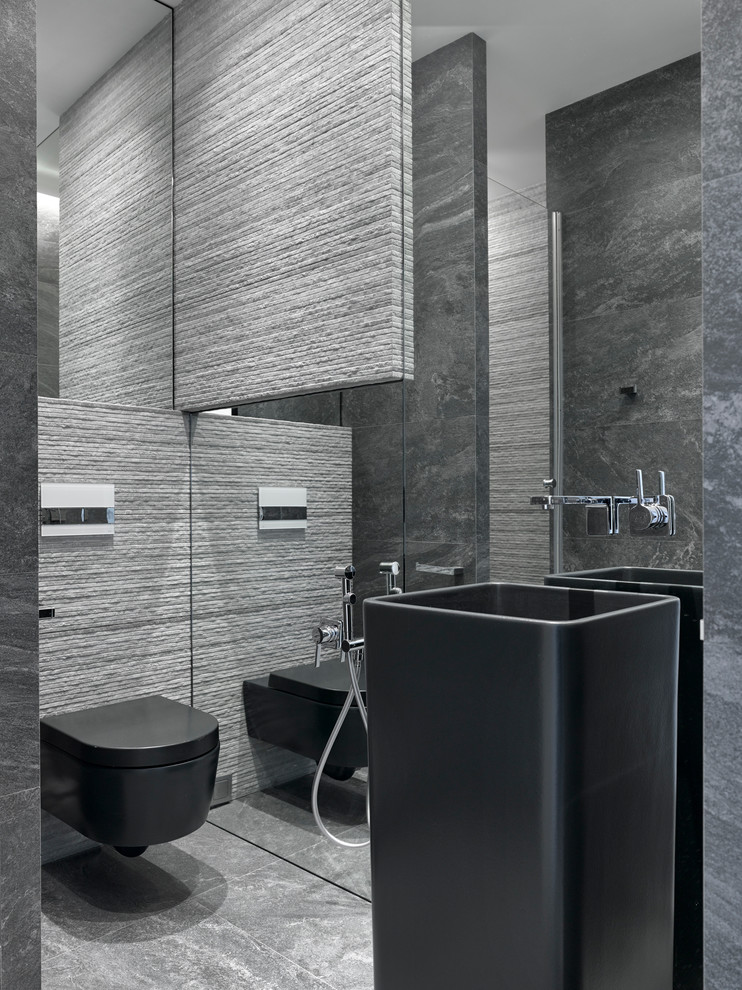 Bild på ett funkis toalett, med ett piedestal handfat, en vägghängd toalettstol och grå kakel