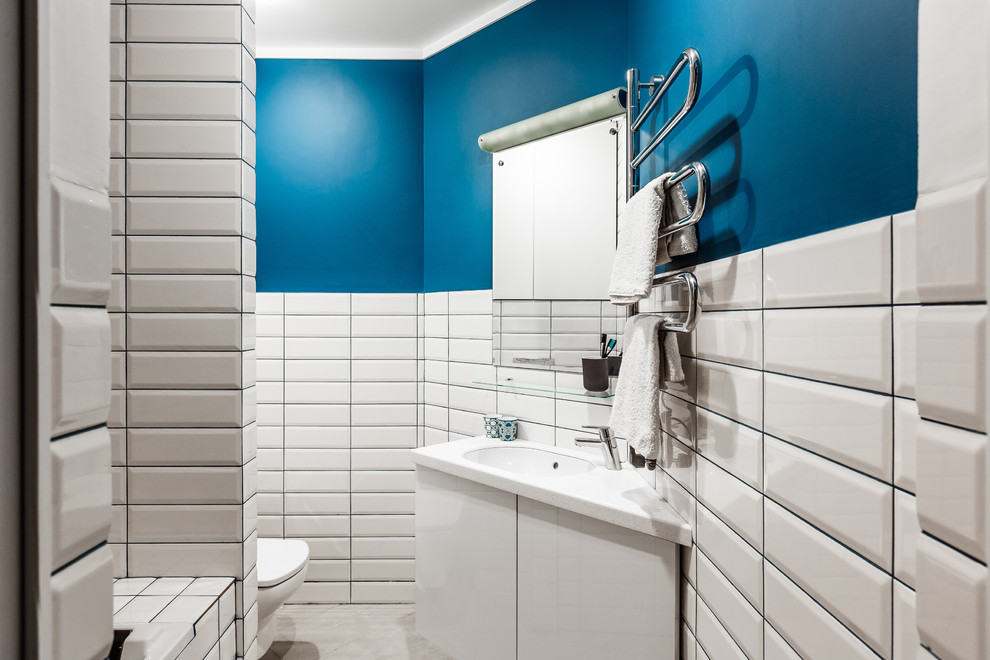 Idée de décoration pour un WC et toilettes design avec un placard à porte plane, des portes de placard blanches, un carrelage blanc, un carrelage métro, un mur bleu, un lavabo encastré et un sol gris.