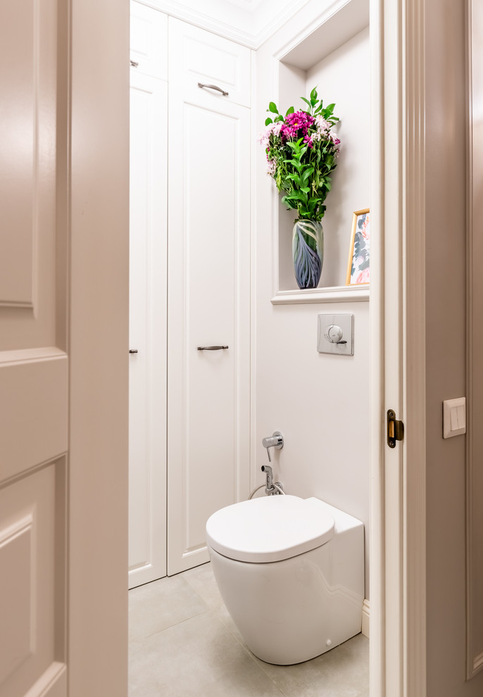 Стильный дизайн: туалет среднего размера в классическом стиле с фасадами с выступающей филенкой, белыми фасадами, инсталляцией, бежевой плиткой, бежевыми стенами, полом из керамической плитки, настольной раковиной и серым полом - последний тренд