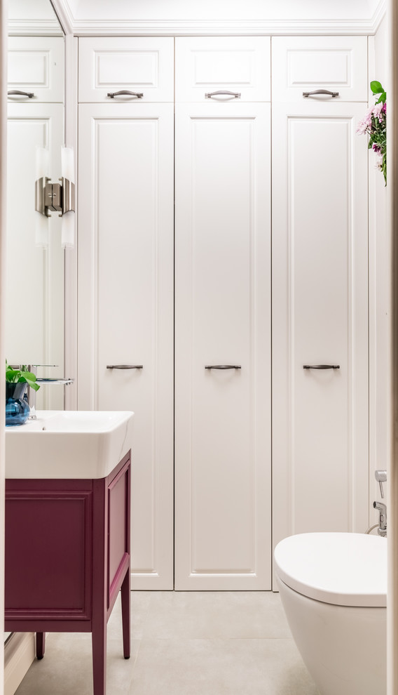 Klassisk inredning av ett mellanstort toalett, med luckor med upphöjd panel, vita skåp, en vägghängd toalettstol, beige kakel, beige väggar, klinkergolv i keramik, ett fristående handfat och grått golv