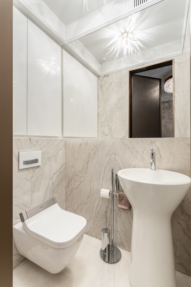 Foto på ett litet funkis toalett, med en vägghängd toalettstol, beige kakel, ett piedestal handfat och beiget golv