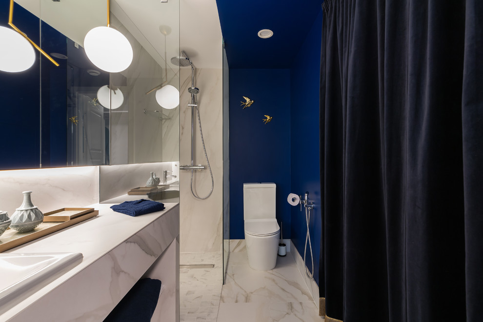 Foto på ett litet skandinaviskt vit toalett, med vita skåp, en toalettstol med separat cisternkåpa, vit kakel, marmorkakel, blå väggar, marmorgolv, ett nedsänkt handfat, marmorbänkskiva och vitt golv