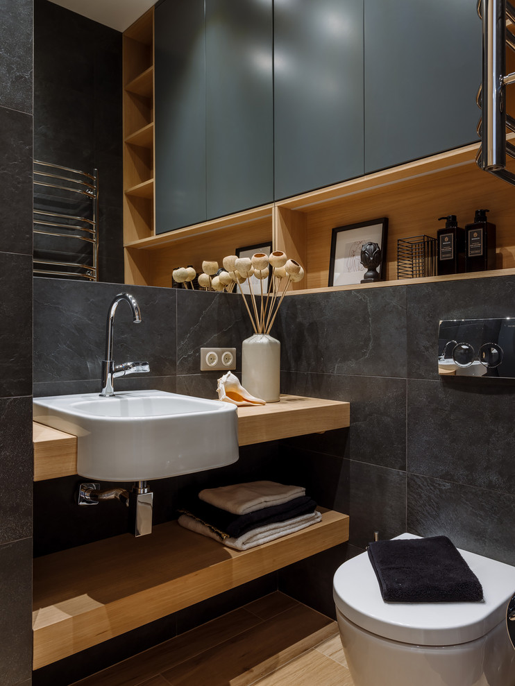 This is an example of a contemporary cloakroom in Moscow with a one-piece toilet, black tiles, a built-in sink, wooden worktops, brown floors, brown worktops and open cabinets.