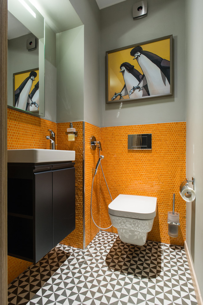 Пример оригинального дизайна: маленький туалет в современном стиле с плоскими фасадами, черными фасадами, инсталляцией, оранжевой плиткой, черно-белой плиткой, плиткой мозаикой, серыми стенами, монолитной раковиной и разноцветным полом для на участке и в саду