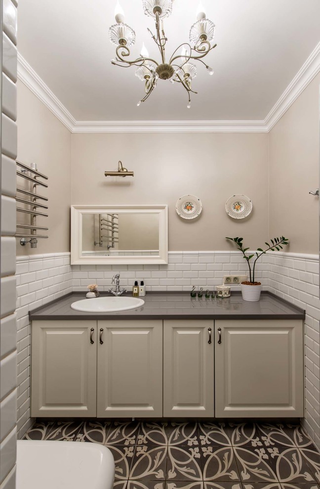 Bild på ett vintage grå grått toalett, med luckor med upphöjd panel, beige skåp, vit kakel, brun kakel, beige väggar, ett nedsänkt handfat och flerfärgat golv