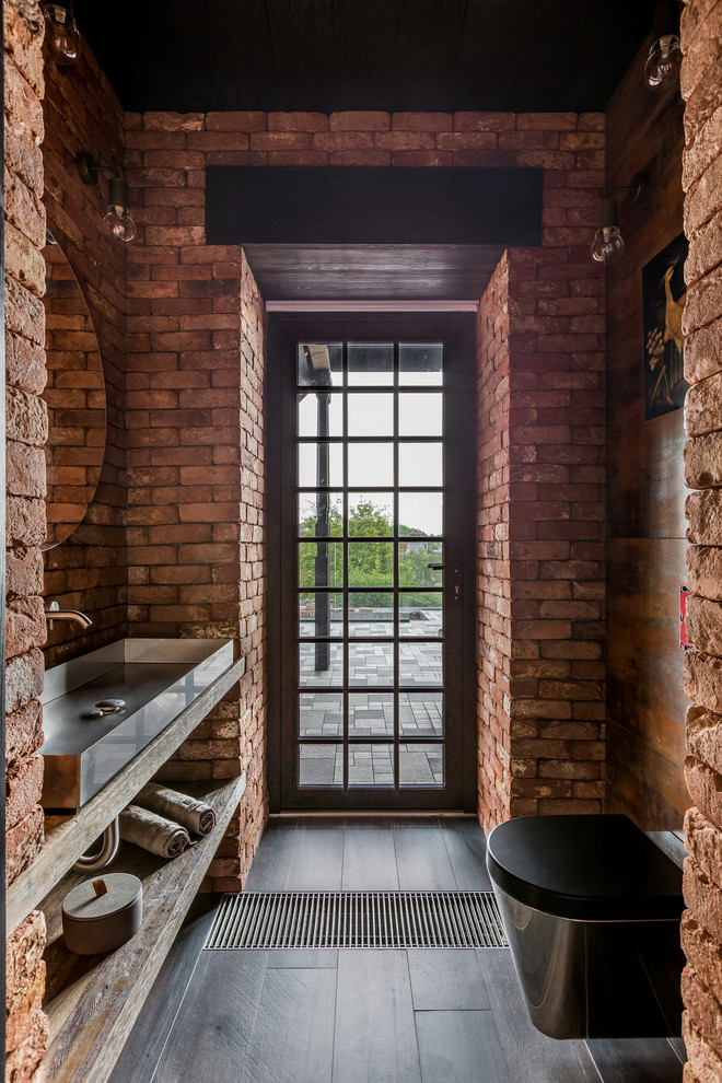 Inspiration pour un WC suspendu urbain en bois clair avec une vasque, un plan de toilette en bois, un sol noir, un placard sans porte, un mur rouge et un plan de toilette beige.