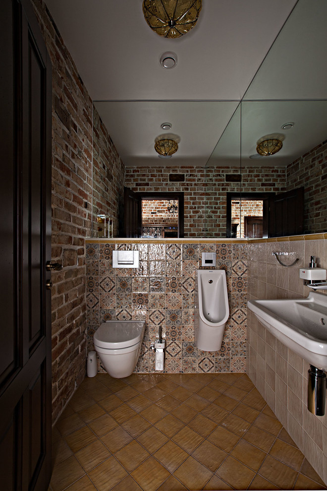Esempio di un bagno di servizio industriale di medie dimensioni con WC sospeso, piastrelle beige, piastrelle in ceramica, pareti beige, pavimento con piastrelle in ceramica, lavabo sospeso e pavimento marrone