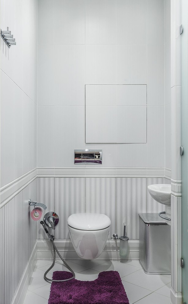This is an example of a small traditional cloakroom in Moscow with a wall mounted toilet, white tiles, white walls, a wall-mounted sink, white floors, ceramic tiles and ceramic flooring.