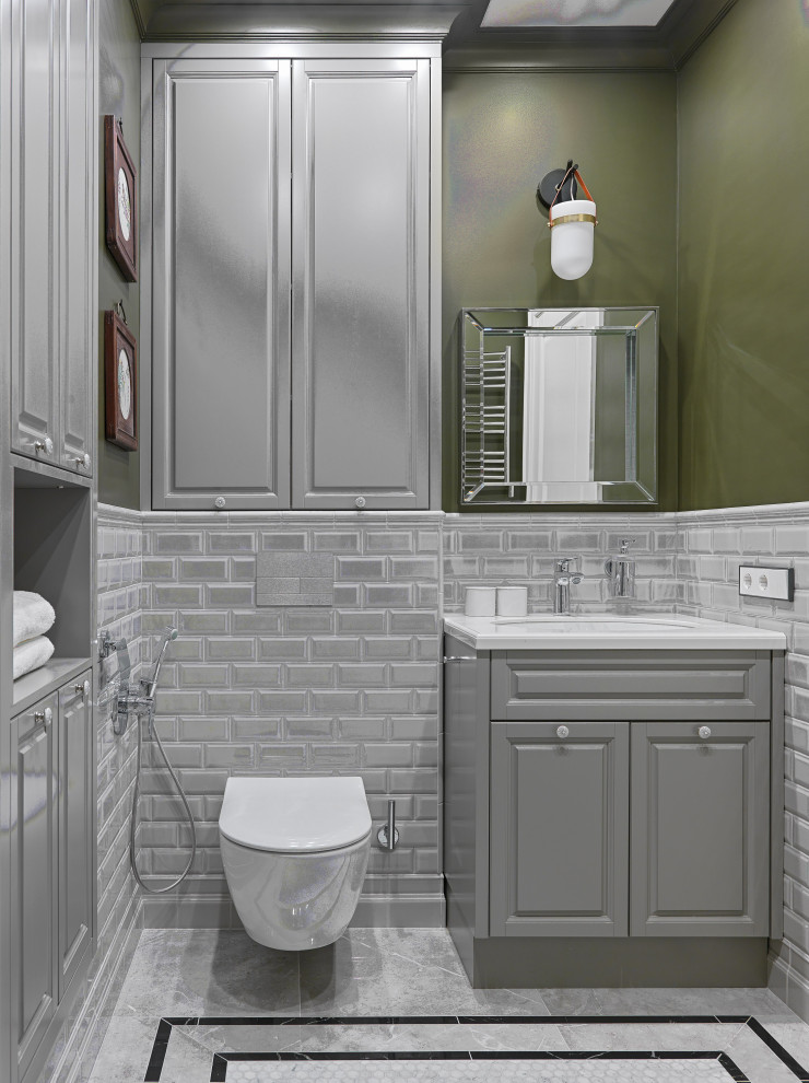 Aménagement d'un WC suspendu classique avec un placard avec porte à panneau surélevé, des portes de placard grises, un carrelage gris, un carrelage métro, un mur vert, un lavabo encastré, un sol gris, un plan de toilette blanc et meuble-lavabo sur pied.