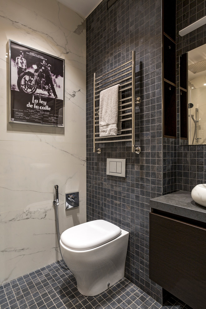 Bild på ett funkis toalett, med en toalettstol med separat cisternkåpa, grå kakel, mosaik, mosaikgolv, ett fristående handfat och grått golv