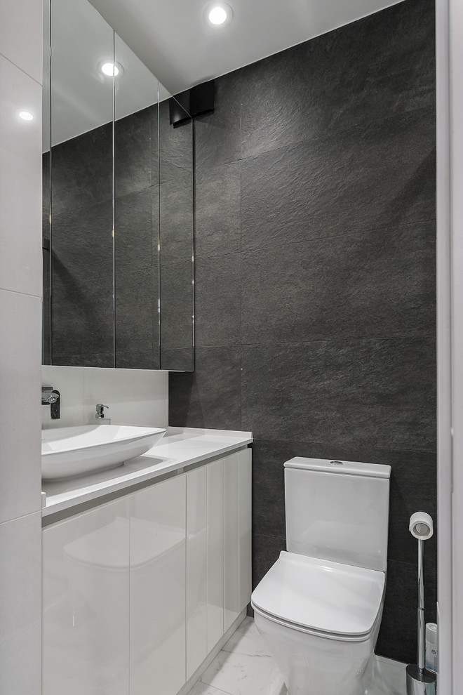 Пример оригинального дизайна: туалет в современном стиле с плоскими фасадами, белыми фасадами, раздельным унитазом, черной плиткой, настольной раковиной и белым полом