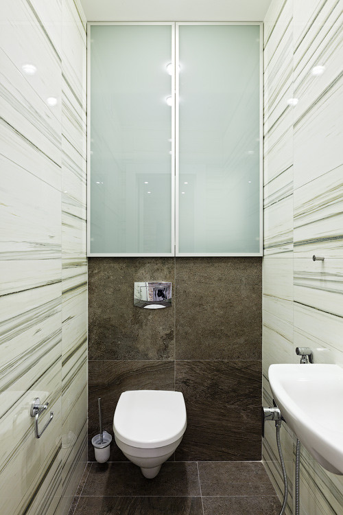 Réalisation d'un petit WC suspendu design avec un placard à porte vitrée, un carrelage blanc, des carreaux de céramique, un sol en carrelage de porcelaine, un lavabo suspendu et un sol marron.