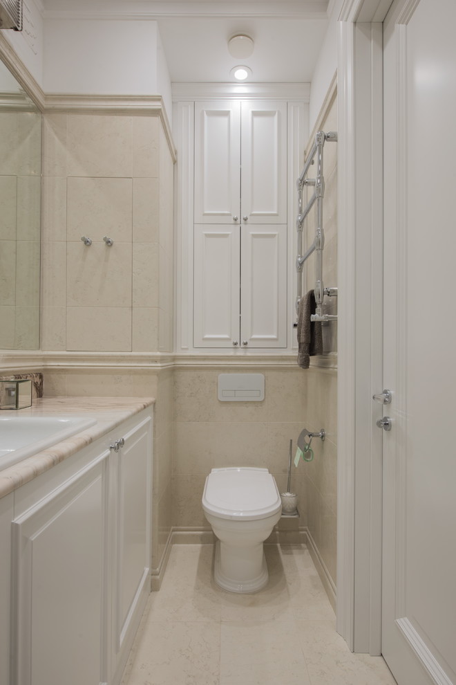 Foto di un bagno di servizio classico con ante con bugna sagomata, ante bianche, WC a due pezzi, piastrelle beige, lavabo da incasso, pavimento beige e top beige