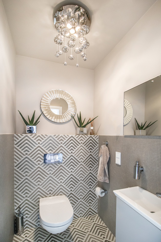 Immagine di un bagno di servizio design con ante grigie, WC sospeso, piastrelle grigie, piastrelle a mosaico, pareti rosa, pavimento con piastrelle a mosaico, lavabo integrato, pavimento grigio e top bianco