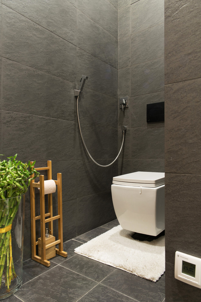 Diseño de aseo actual con sanitario de pared, baldosas y/o azulejos negros y suelo gris