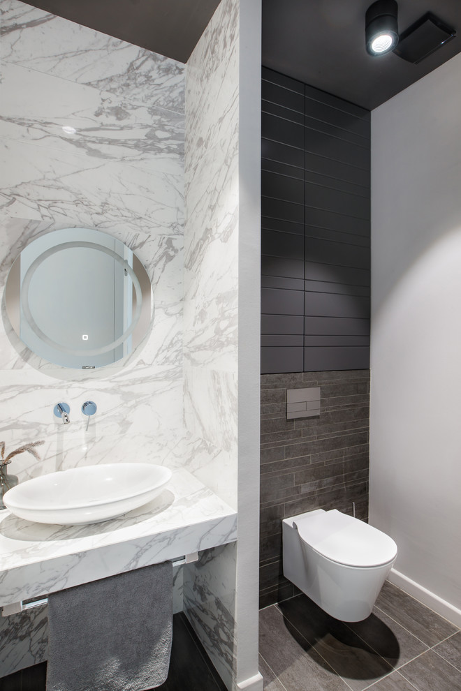 Small contemporary cloakroom in Yekaterinburg with a wall mounted toilet, white tiles, marble tiles, white walls, a vessel sink, marble worktops, grey floors, white worktops and feature lighting.