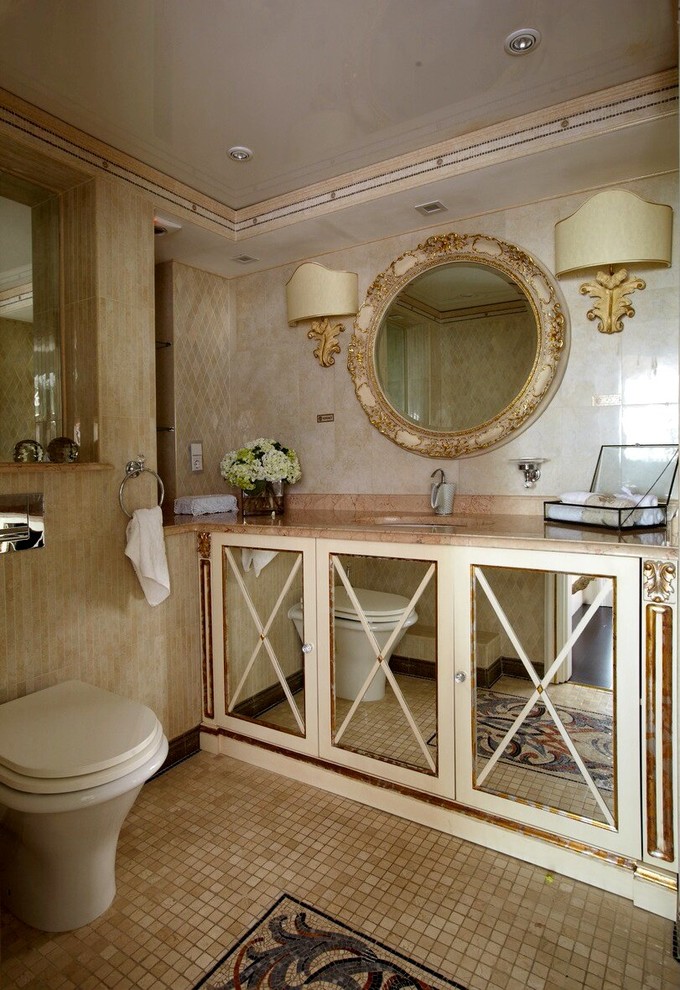 Klassisk inredning av ett toalett, med luckor med glaspanel, en toalettstol med separat cisternkåpa, beige kakel, ett undermonterad handfat och beiget golv