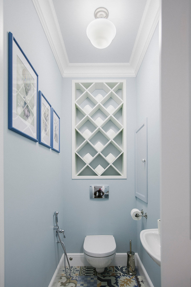 Modelo de aseo clásico renovado con sanitario de pared, lavabo suspendido, paredes azules, suelo de azulejos de cemento y suelo multicolor