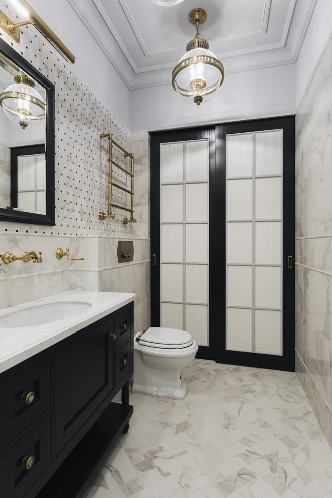 Immagine di un bagno di servizio classico con ante con riquadro incassato, ante nere, WC a due pezzi, piastrelle beige, lavabo sottopiano, pavimento beige e top bianco