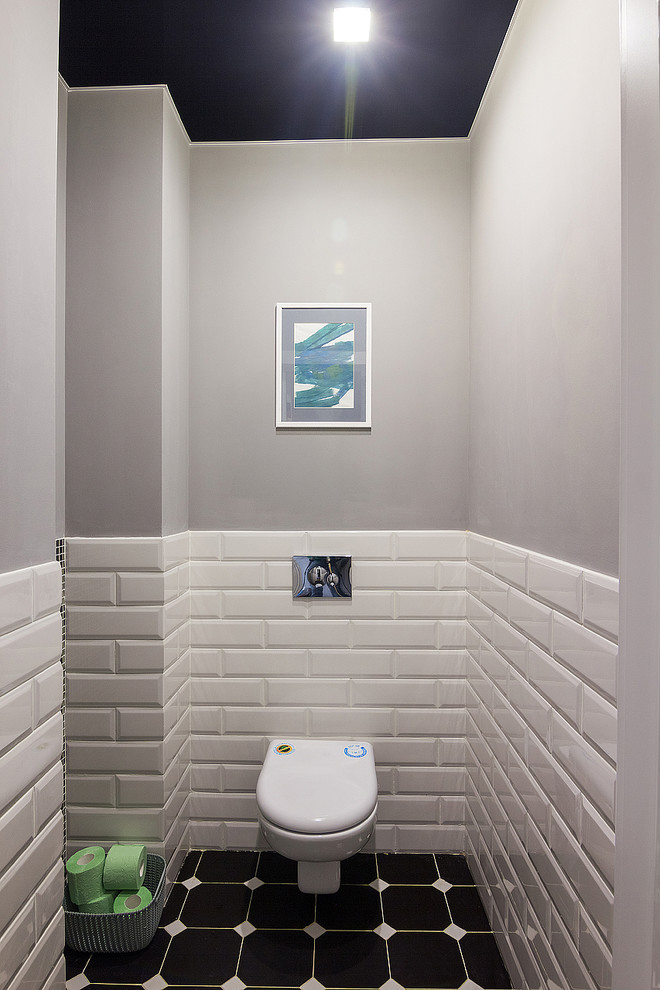 Bild på ett litet industriellt toalett, med en vägghängd toalettstol, stickkakel, grå väggar, klinkergolv i porslin och svart golv