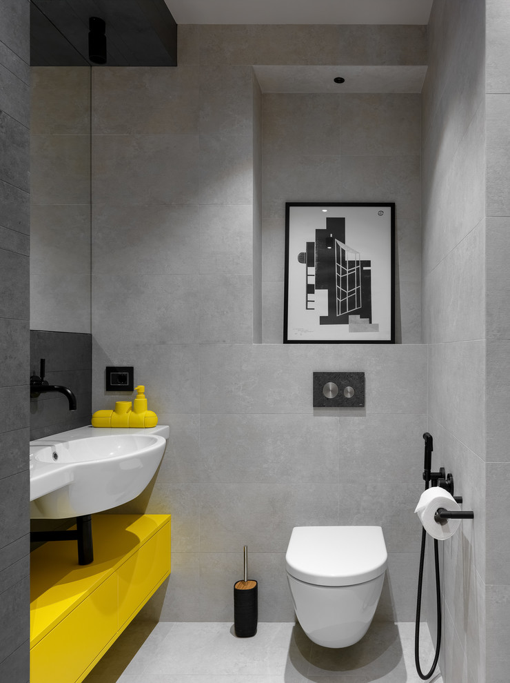 Réalisation d'un WC suspendu design avec un placard à porte plane, des portes de placard jaunes, un carrelage gris, un lavabo intégré, un sol gris et un plan de toilette blanc.