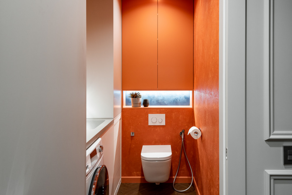 Photo of a small modern cloakroom in Yekaterinburg with flat-panel cabinets, orange cabinets, a wall mounted toilet, orange walls, vinyl flooring, a submerged sink, solid surface worktops, beige floors, grey worktops and a built in vanity unit.