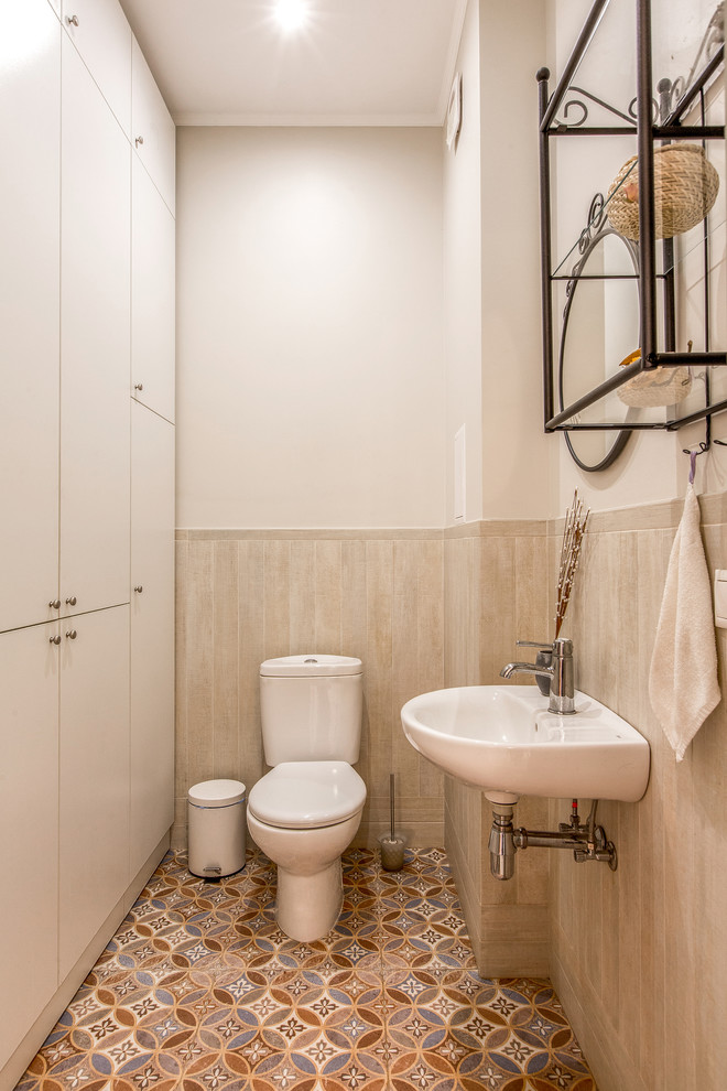 Foto på ett vintage toalett, med en toalettstol med separat cisternkåpa, ett väggmonterat handfat, flerfärgad kakel, beige väggar och flerfärgat golv
