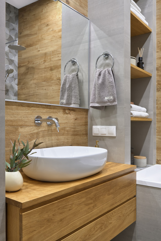 Foto på ett litet funkis beige toalett, med släta luckor, skåp i ljust trä, beige kakel, grå väggar, ett fristående handfat och träbänkskiva